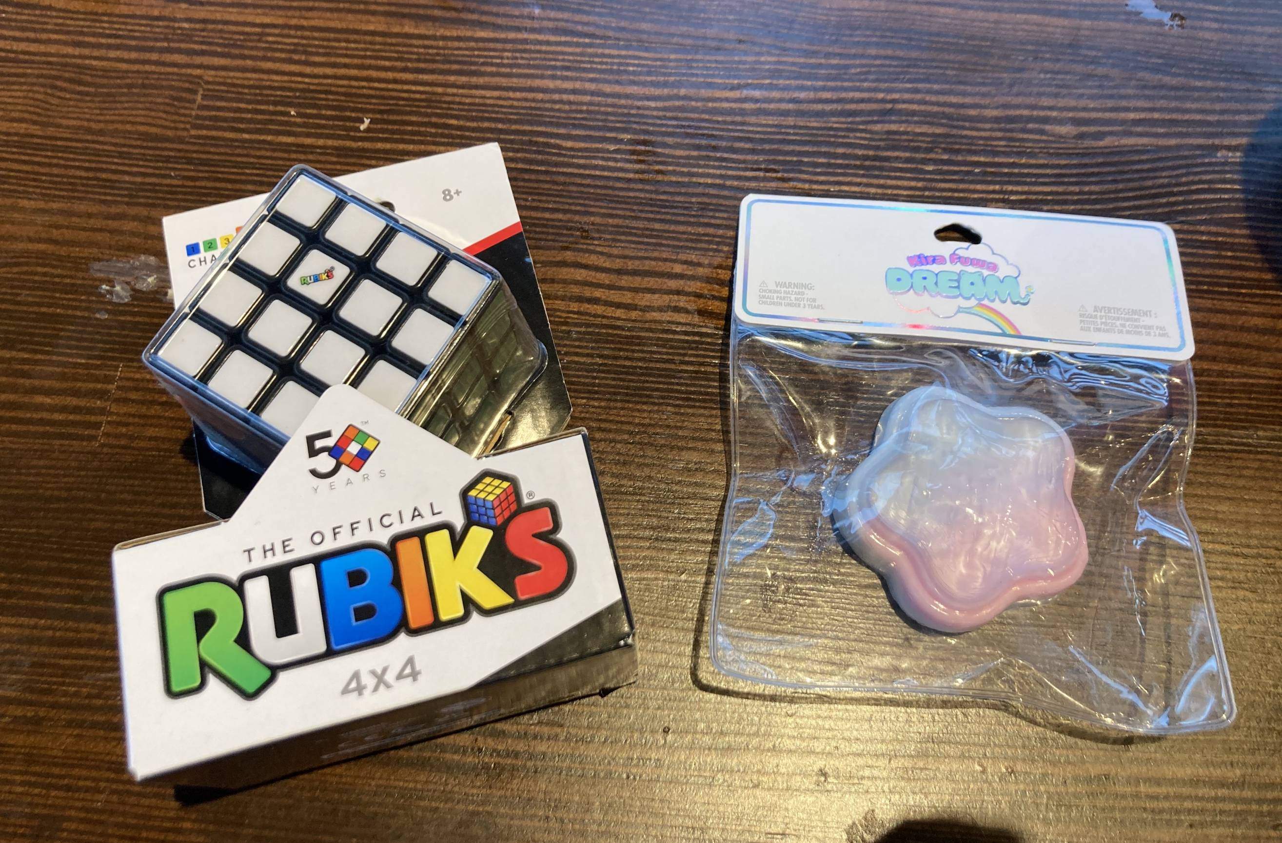 A 4x4 Rubik's Cube still in it's box and a pink and blue star-shaped taba squishy on a table.