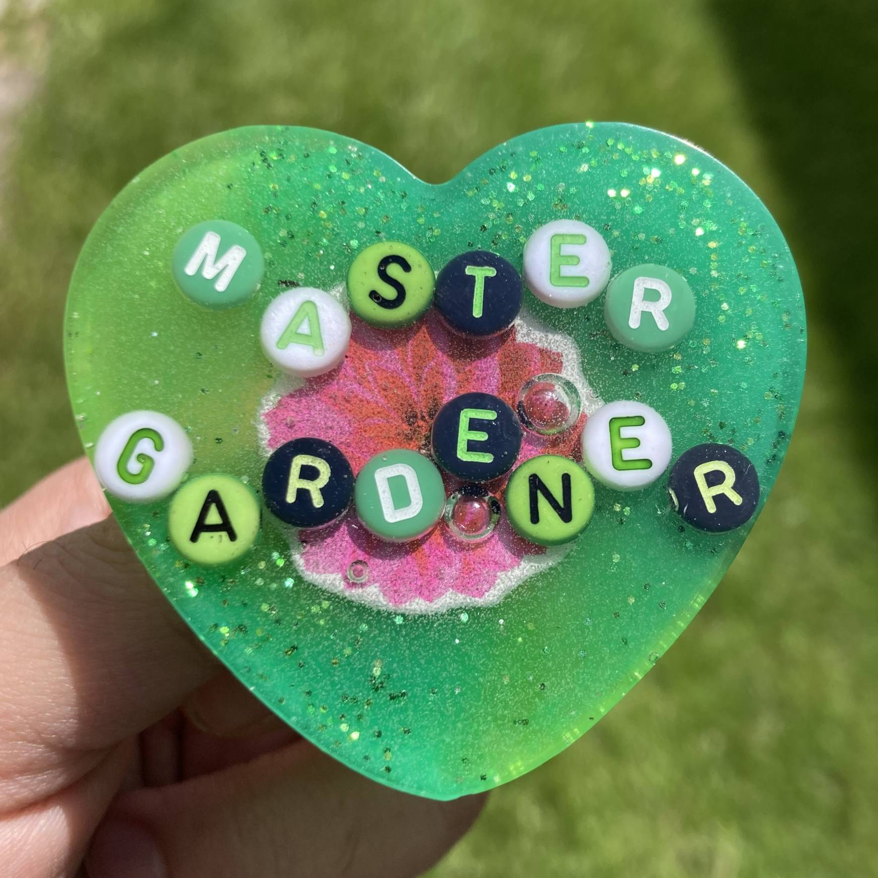 A green, heart-shaped resin pin that says 'Master Gardener'.