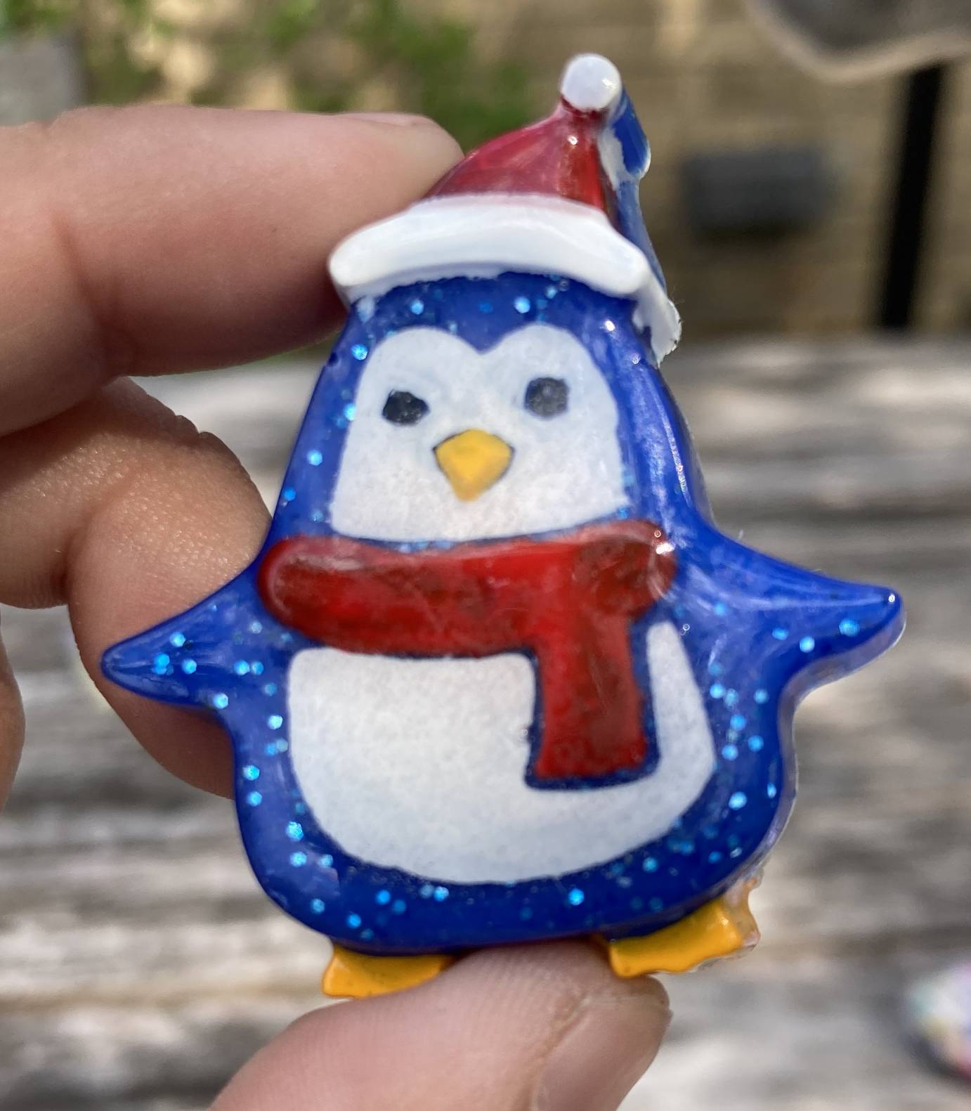 A blue resin penguin wearing a red scarf and santa hat.
