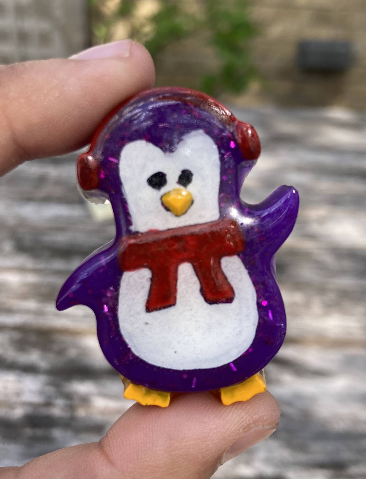 A purple resin penguin wearing a red scarf and earmuffs.