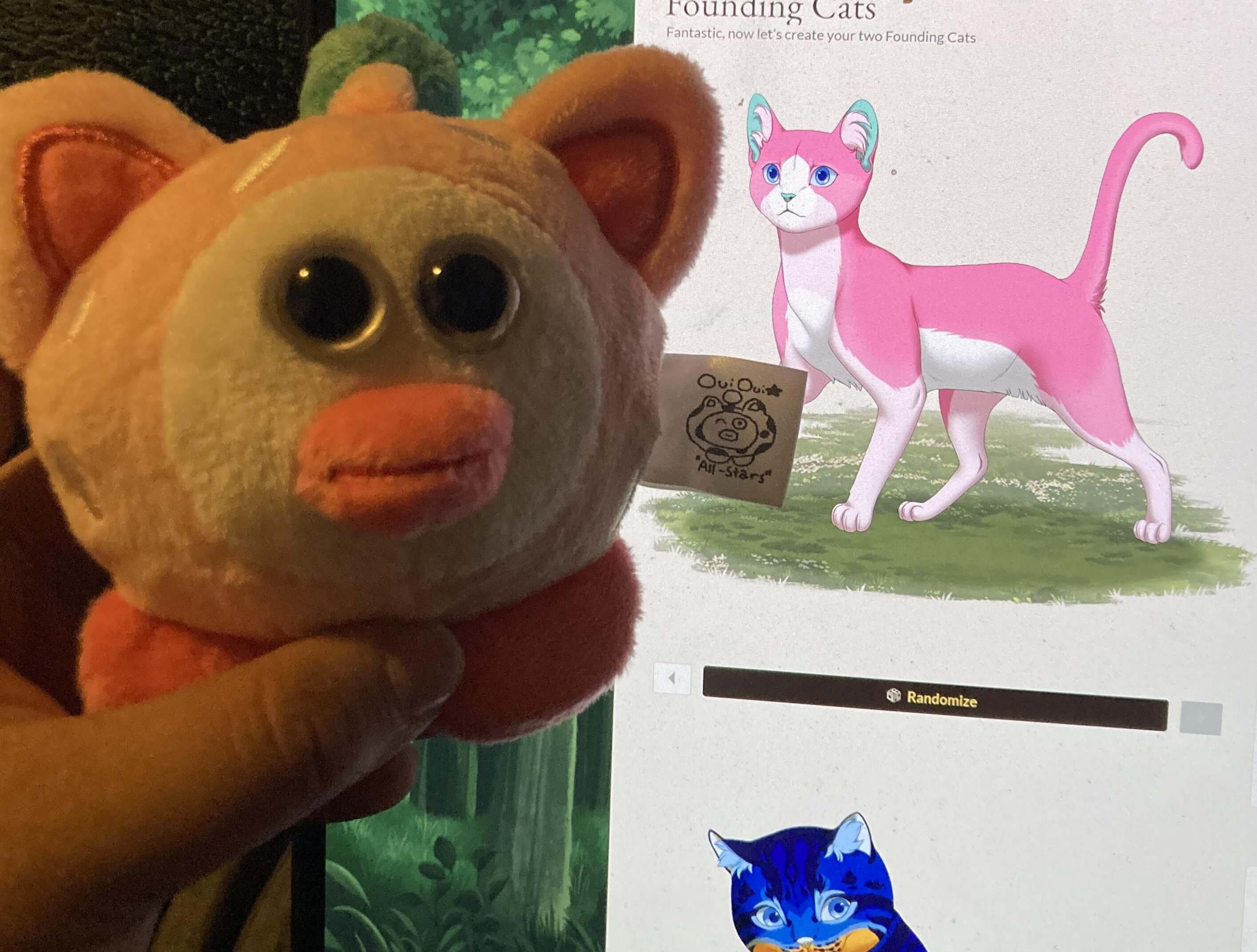 Strawberry OuiOui without its strawberry outfit on being held up in front of my computer monitor, which shows a cartoon pink and white cat.